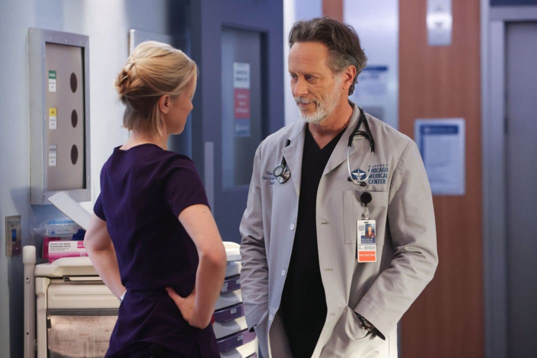 Imagen promocional de "Chicago Med" 9x05 Hannah de espaldas habla con Archer en el pasillo del hospital